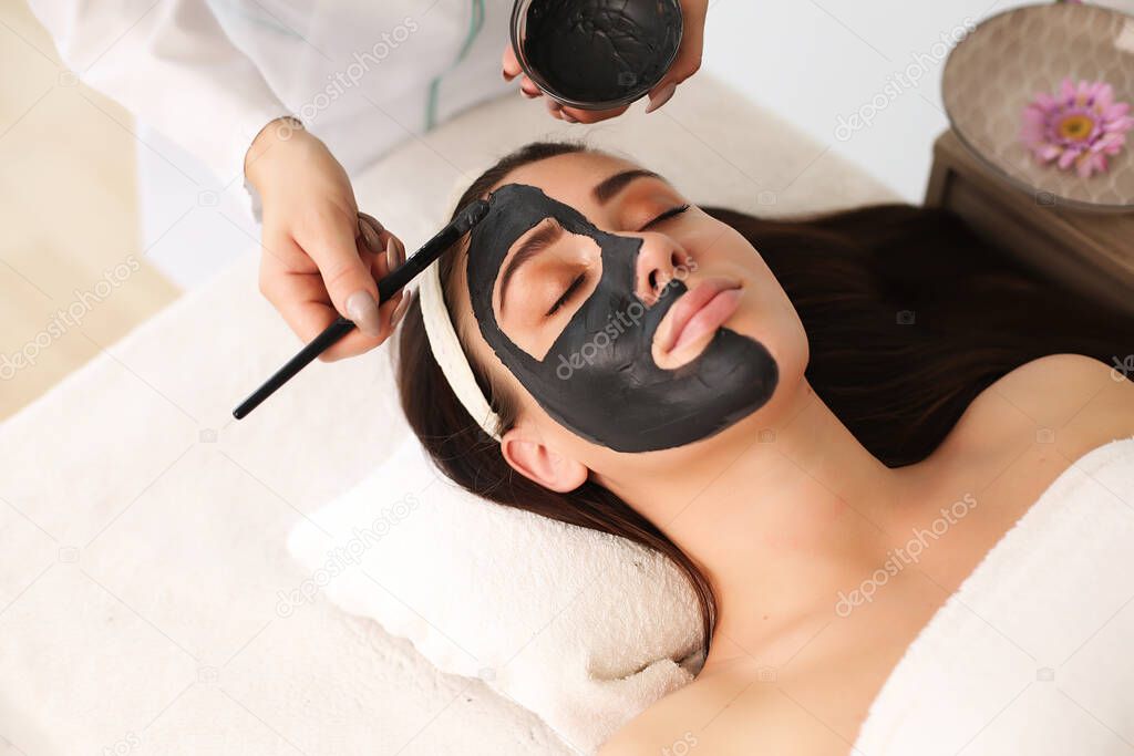 The hands of a cosmetologist apply a mask on the face with a brush, making the skin moisturized and the face glow and skin.