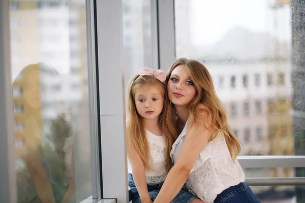 Mother and her baby girl playing hugging against the backdrop of a panoramic window — Stock Photo, Image