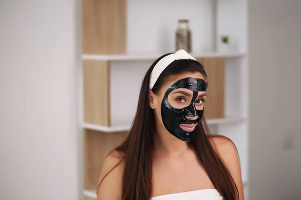 Mladá žena s uhlíkovou detoxikační černou maskou na obličeji, dospívající dívka se stará o mastnou pleť, čistí póry. Kosmetický salon. Péče o kůži. — Stock fotografie