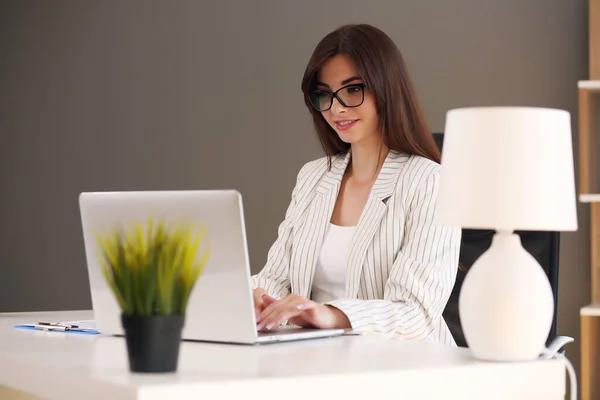 Mulher de negócios bonita usa um laptop e sorri enquanto trabalha no escritório — Fotografia de Stock