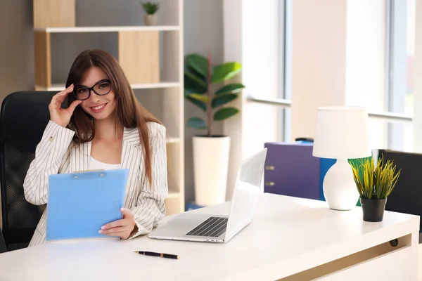 Mulher de negócios bonita usa um laptop e sorri enquanto trabalha no escritório — Fotografia de Stock