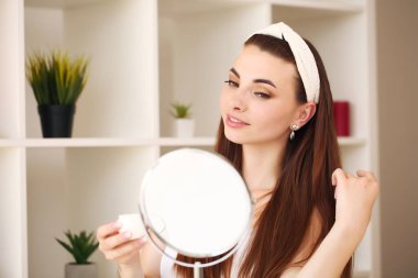 Duştan sonra banyoda çekici genç bir kadın aynanın önünde yüz kremiyle duruyor. Kadınlar umursar.