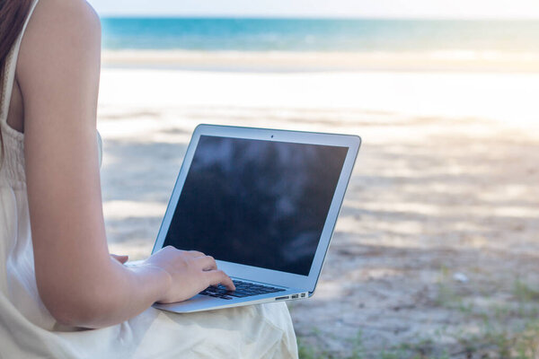Young Asian woman using laptop in dress sitting on the beach,Gir