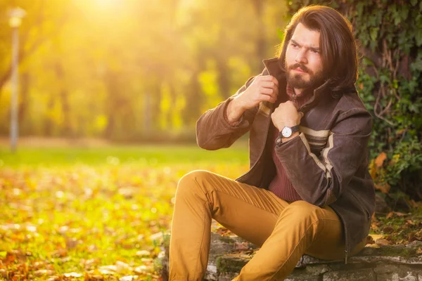 Sonbahar ormanda yakınındaki taş üzerinde oturan yakışıklı adam   