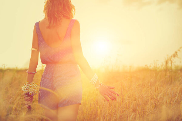 женщина в голубой одежде с букетом цветов, касающихся ушей ячменя во время прогулки по лугу в солнечный день
