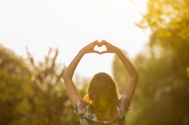 arkadan görünüşü kaldırdı elleriyle ayakta ve kalp işareti ormanda güneş doğarken gösterilen kadın