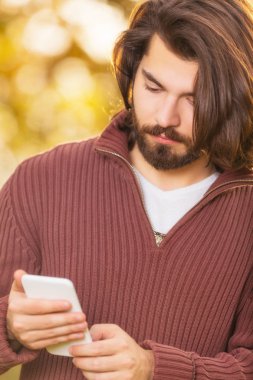 yakışıklı adam arka plan üzerinde bulanık sonbahar orman ile Smartphone kullanarak 