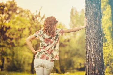 arkadan görünüşü kadın ormanda ağaç gövdesi üzerine eğilerek yaz giysileri 