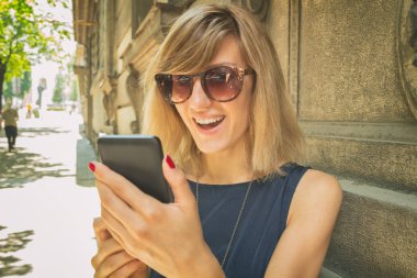 mutlu gülümseyen kadın bulanık Caddesinde duran smartphone kullanarak güneş gözlüğü 