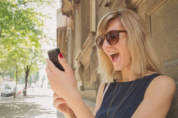 mutlu gülümseyen kadın bulanık Caddesinde duran smartphone kullanarak güneş gözlüğü 