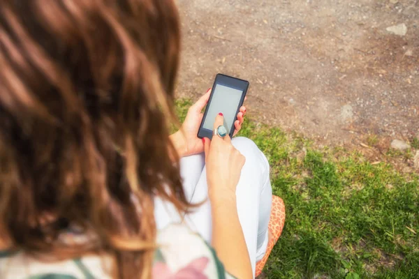 Parkta otururken Smartphone kullanarak yazlık giysiler giyen kadın