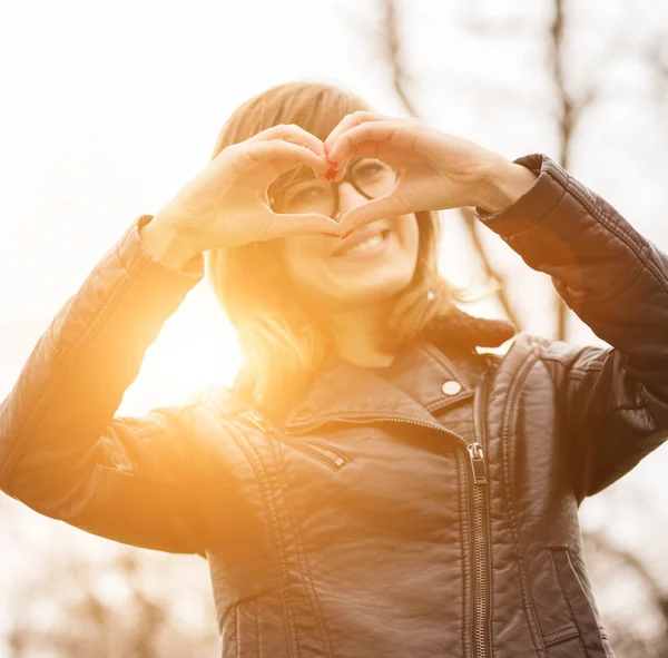 kameraya bakarak ve kalp işareti ormanda günbatımında gösterilen sevimli kadın 