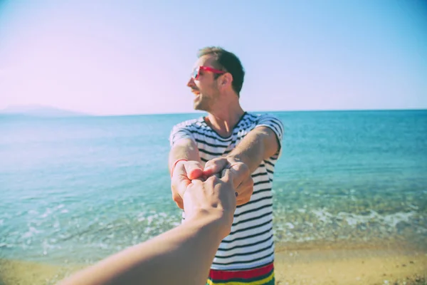 Man holding hand of his girlfriend on the beach. Focus is on the hands.