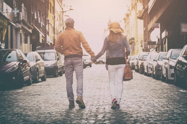back view of sweet couple holding hands and walking along street