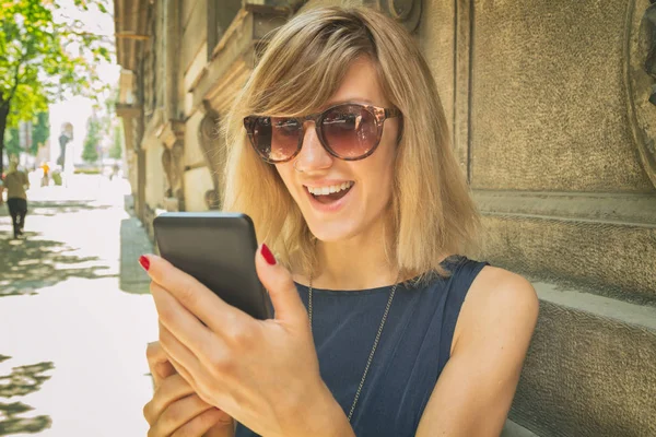 mutlu gülümseyen kadın bulanık Caddesinde duran smartphone kullanarak güneş gözlüğü 