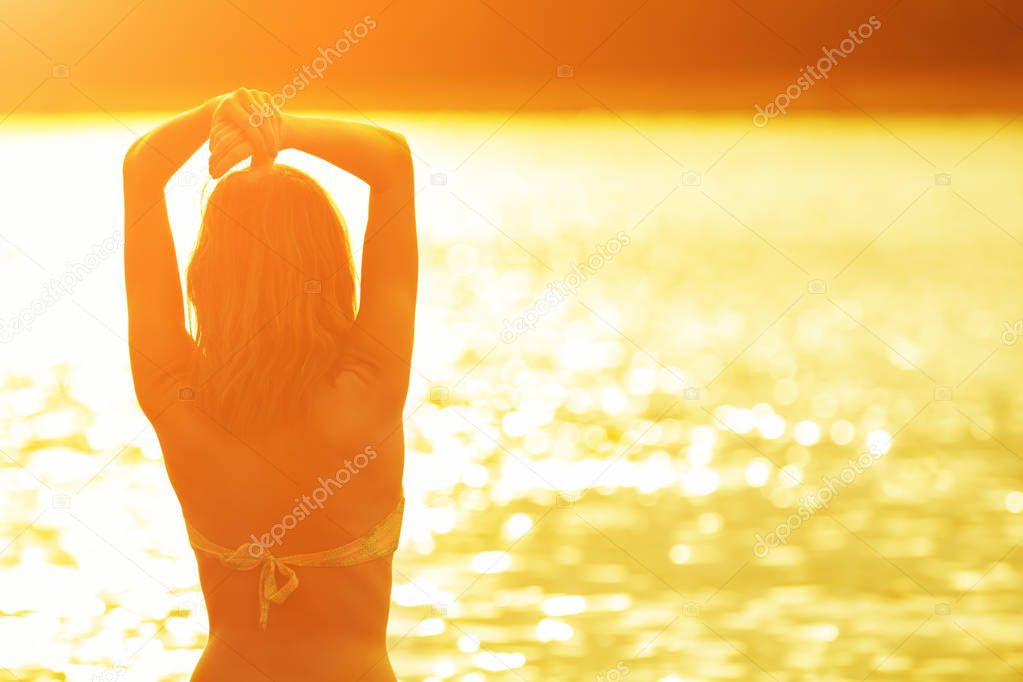back view of woman standing at seashore at orange fiery sunset 