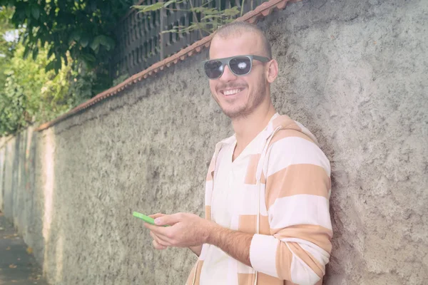 Hombre Sonriente Usando Teléfono Inteligente Mientras Apoya Pared Hormigón Calle —  Fotos de Stock