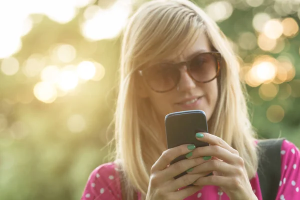 Γυναίκα Γυαλιά Ηλίου Πληκτρολόγηση Smartphone Ενώ Στέκεται Στην Θολή Φόντο — Φωτογραφία Αρχείου