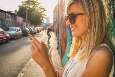 Street arka plan üzerinde patenci ile Smartphone grafiti duvarının yakınında dururken kullanan kadın 