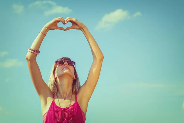 Usmívající Žena Sluneční Brýle Rukou Ukazující Znamení Srdce Proti Modré — Stock fotografie