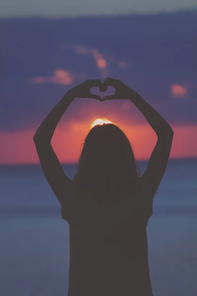 Girl making heart shape with hands at the beach