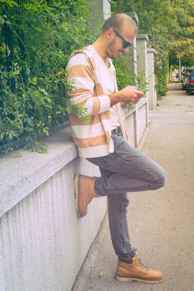 Hombre Sonriente Usando Teléfono Inteligente Mientras Apoya Pared Hormigón Calle —  Fotos de Stock