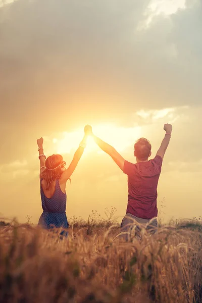 happy man with woman holding raised hands on meadow at sunset