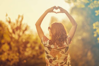 arkadan görünüşü kaldırdı elleriyle ayakta ve kalp işareti ormanda güneş doğarken gösterilen kadın
