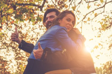 gülümseyen güzel kadın ve başparmak sonbahar ormanda günbatımı göstermek yukarıya sarılma mutlu yakışıklı adam 