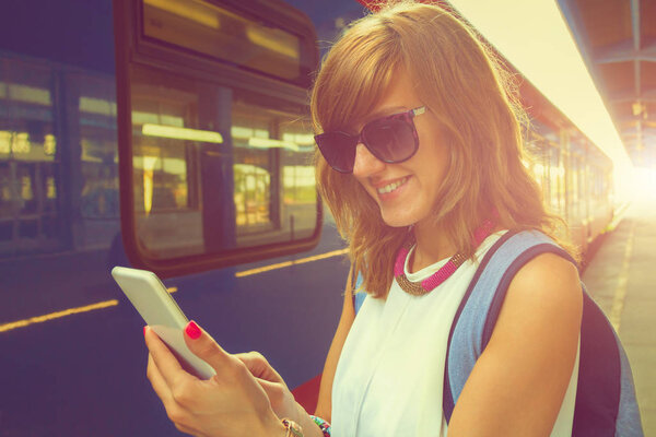 woman using smartphone while standing near train at station 