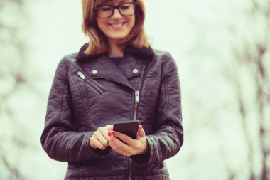 gözlük ve smartphone duran bulanık doğal zemin üzerine yazarak ceket giyen kadın 