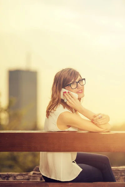 Vrouw Zittend Houten Bankje Met Stadsgezicht Achtergrond Smartphone Park Spreken — Stockfoto