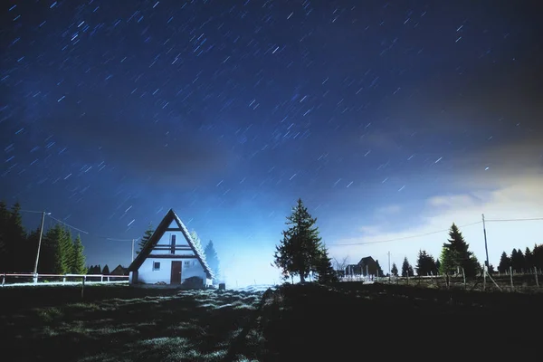 bright stars shining in night sky over dark silhouettes of trees and alone house,