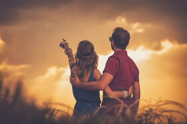 女性は男を抱きしめると夕暮れの草原の空で指を指す — ストック写真