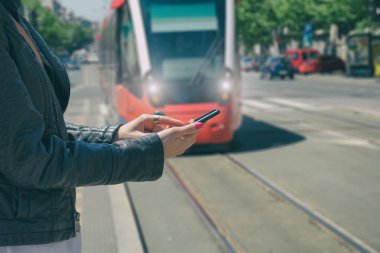 arka plan üzerinde bulanık tramvay ile smartphone istasyonda dururken yazarak eller 