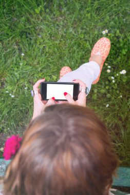 Park yeşil çimenlerin üzerinde otururken Smartphone kullanarak yazlık giysiler giyen kadın