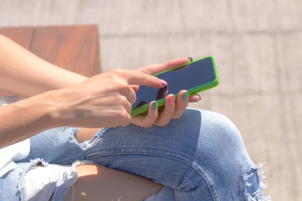 woman wearing summer clothes sitting on bench and using smartphone at street