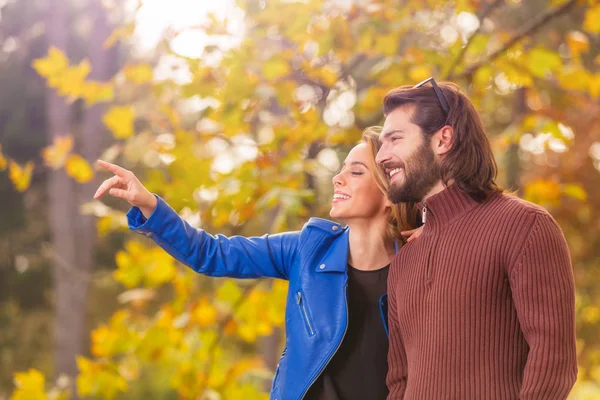 gülümseyen yakışıklı adamla ayakta ve uzağa işaret sonbahar parkta güzel kadın   