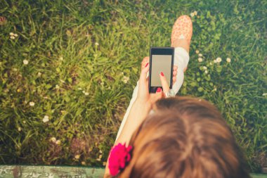 Park yeşil çimenlerin üzerinde otururken Smartphone kullanarak yazlık giysiler giyen kadın