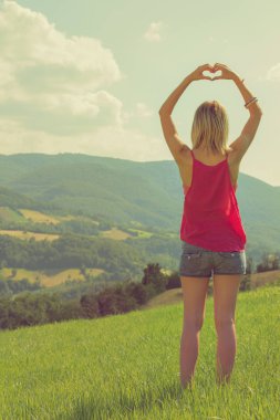 arkadan görünüşü kadın kalp işareti güneşli gün içinde yeşil çim gösterilen kaldırdı elleriyle 