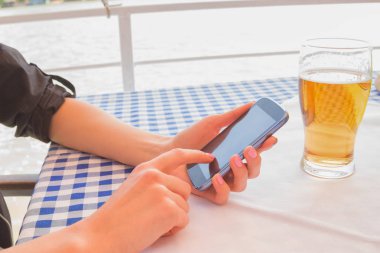 Smartphone ile bardak bira Café, masada otururken kullanan kadın yakın çekim