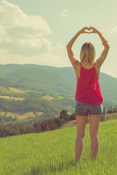 arkadan görünüşü kadın kalp işareti güneşli gün içinde yeşil çim gösterilen kaldırdı elleriyle 