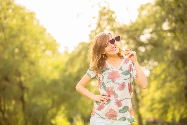 kalp şeklinde gözlük ile tutarak ve parkta poz yazlık elbise giyen sevimli kadın  