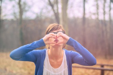 sevimli kadın kalp işareti ormanda günbatımında gösterilen. 