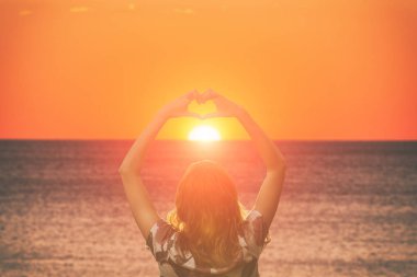 arkadan görünüşü kadın kalp işareti turuncu ateşli batımında, deniz kıyısı dururken gösterilen kaldırdı elleriyle 