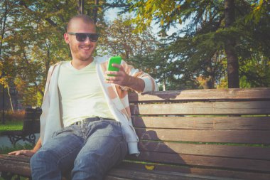 Sonbahar Park ahşap bankta otururken Smartphone kullanan adam 
