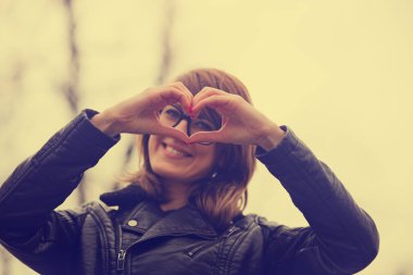 kameraya bakarak ve kalp işareti ormanda günbatımında gösterilen sevimli kadın 