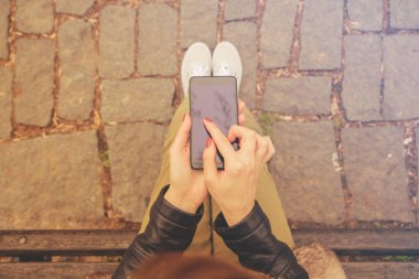 bankta oturan ve sokak, en iyi manzaraya smartphone kullanarak kadın  