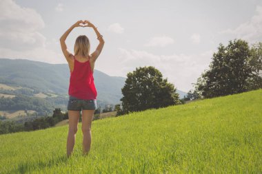 arkadan görünüşü kadın kalp işareti güneşli gün içinde yeşil çim gösterilen kaldırdı elleriyle 