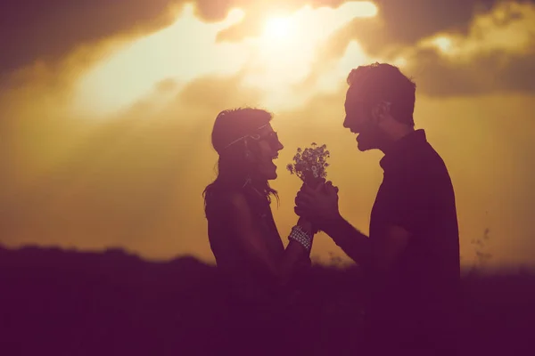 夕暮れ時の牧草地に手を繋いでいるワイルドフラワーの花束と幸せな甘いカップル — ストック写真